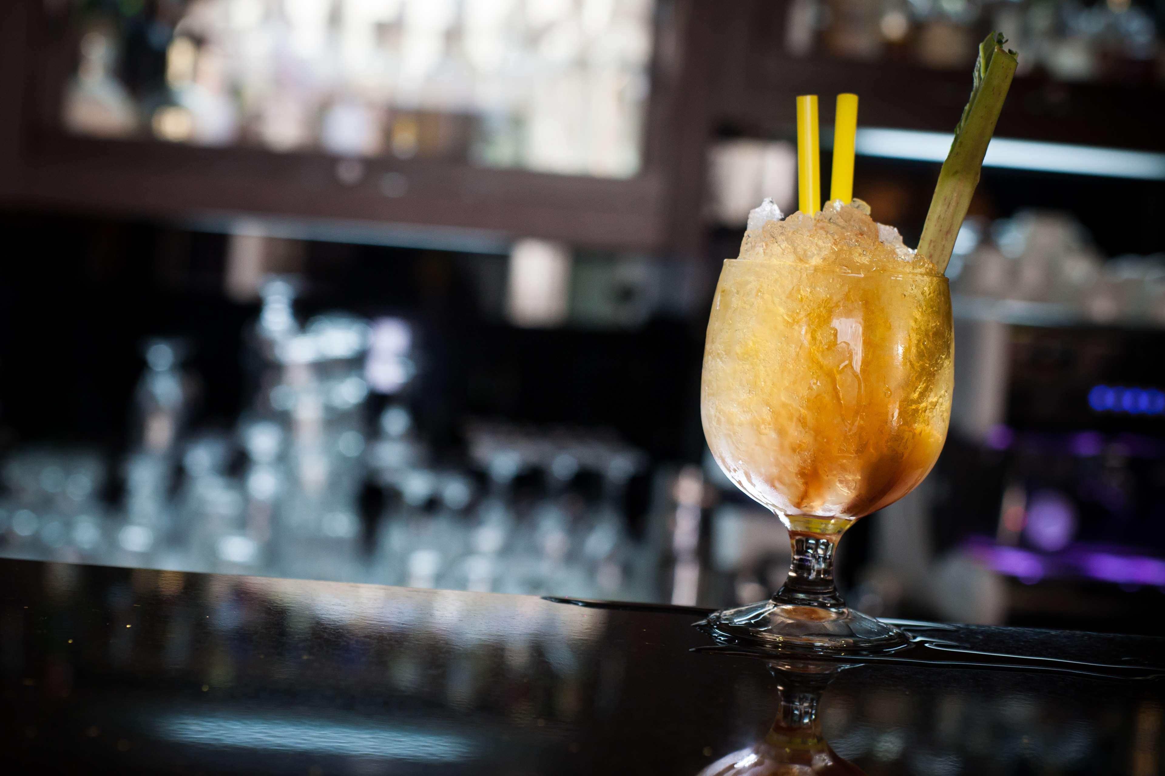 Radisson Blu Hotel, Gdansk Bagian luar foto The photo shows a cocktail served in a decorative glass. The drink appears to be slushy or frozen, with a yellow-orange hue and topped with crushed ice. It has two yellow straws and a piece of celery as garnish. The setting suggests it is in a bar or