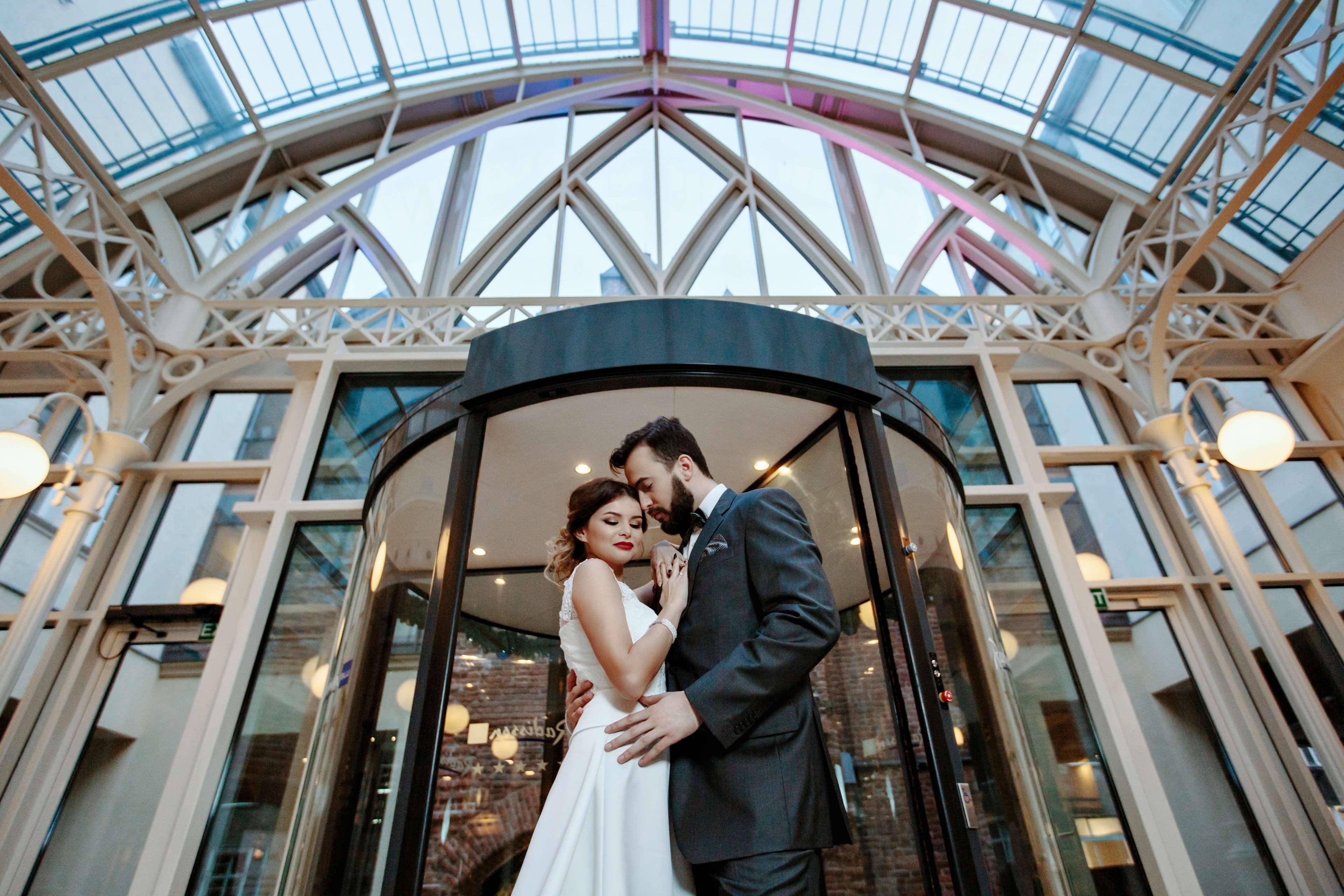 Radisson Blu Hotel, Gdansk Bagian luar foto The photo shows a romantic scene featuring a couple in formal attire, likely celebrating their wedding. They are positioned in front of a round glass door, which is partially open. The couple is standing close together, with their foreheads touching,