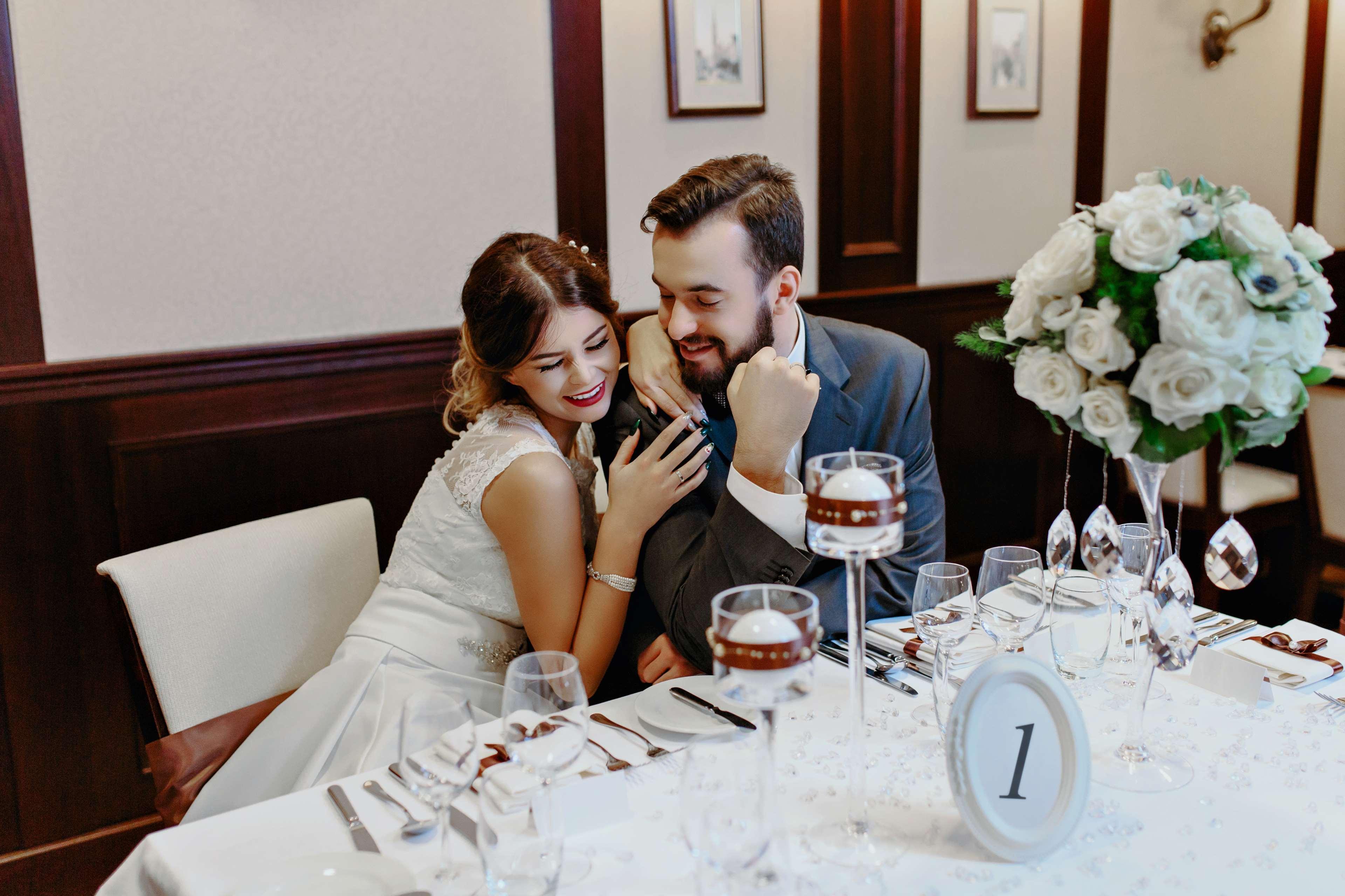 Radisson Blu Hotel, Gdansk Bagian luar foto The photo depicts a couple sitting at a beautifully arranged dining table. The woman, dressed in a white wedding gown, leans affectionately towards the man, who is wearing a gray suit. They appear to be enjoying a moment together, smiling and engagin