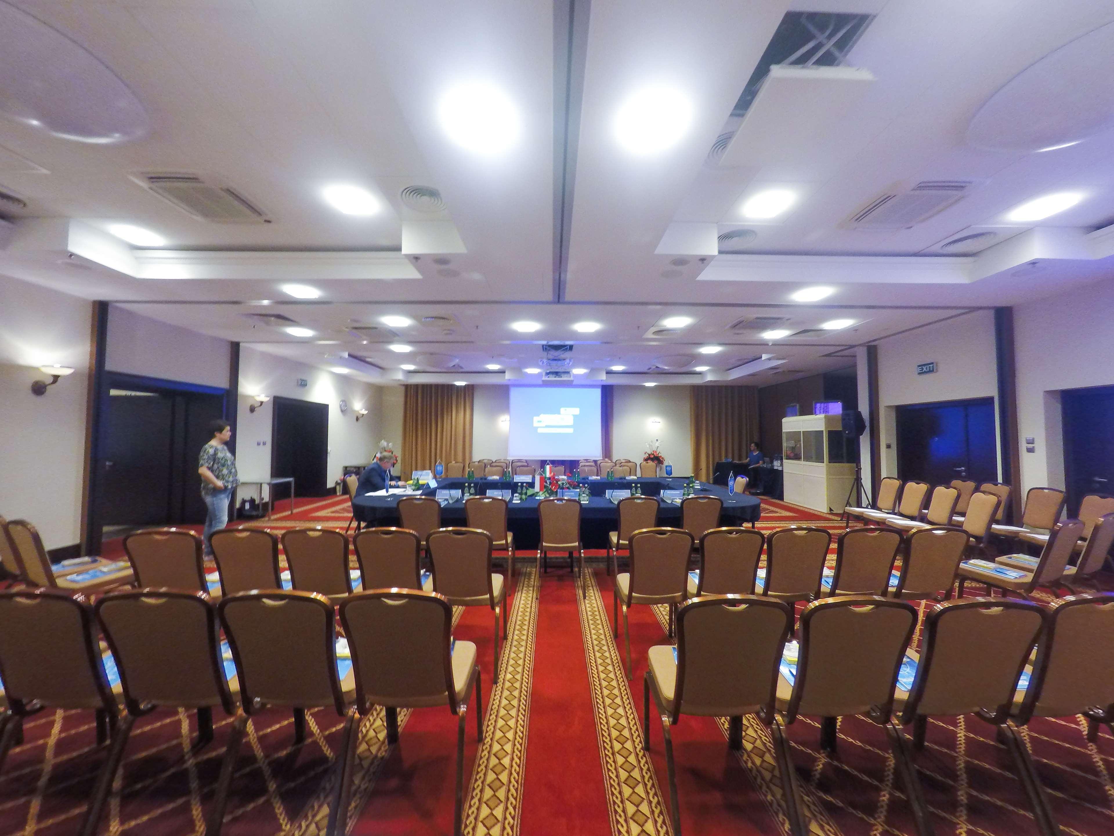 Radisson Blu Hotel, Gdansk Bagian luar foto The photo shows a conference room set up for a meeting or presentation. There are several rows of beige chairs arranged in front of a long table, which is also set up for participants. A large screen or projector is positioned at the front of the roo