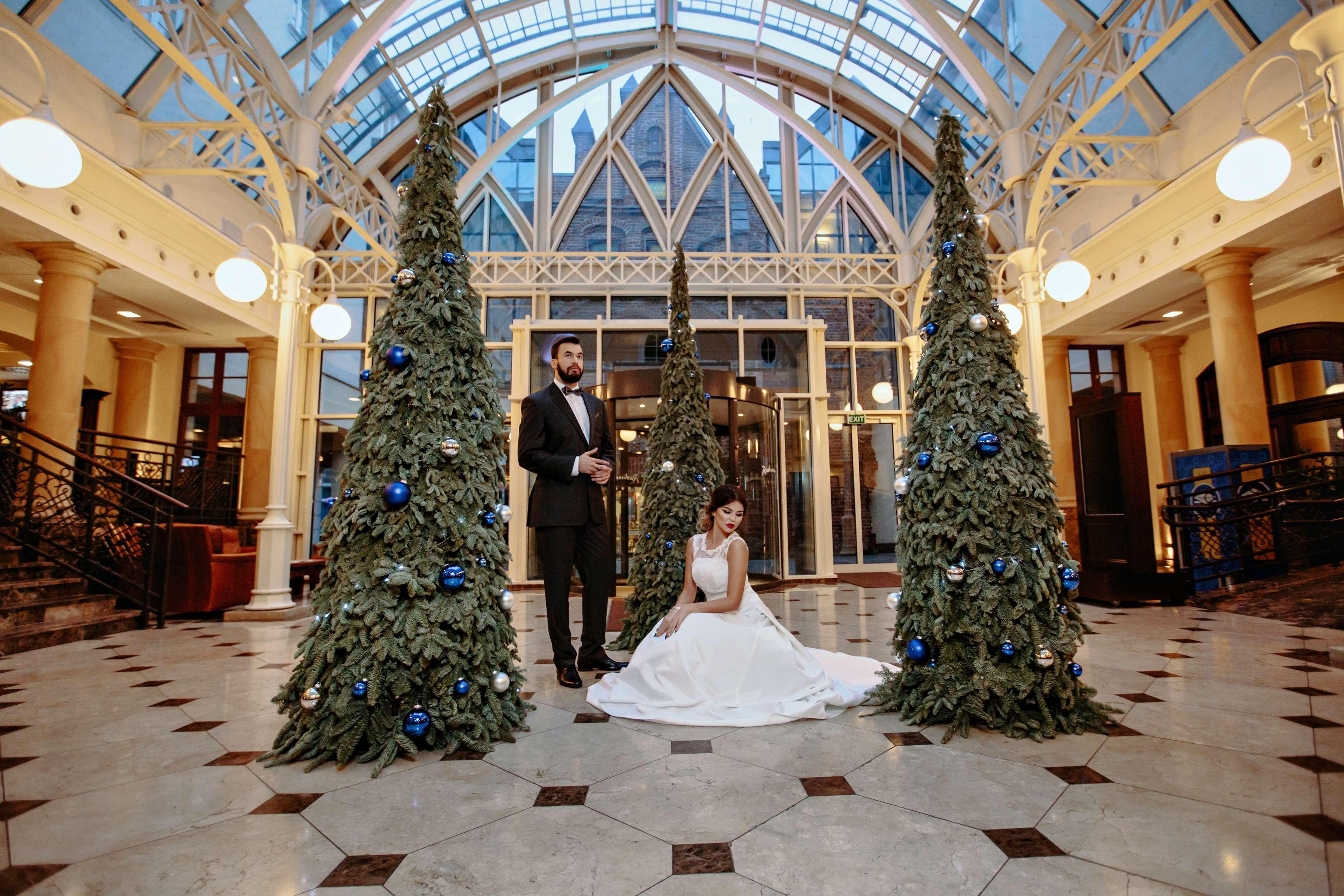 Radisson Blu Hotel, Gdansk Bagian luar foto The photo shows a groom in a tuxedo standing next to a bride in a white wedding dress. They are positioned in a beautifully decorated indoor space, which features large glass windows and elegant architectural details. Surrounding them are three green