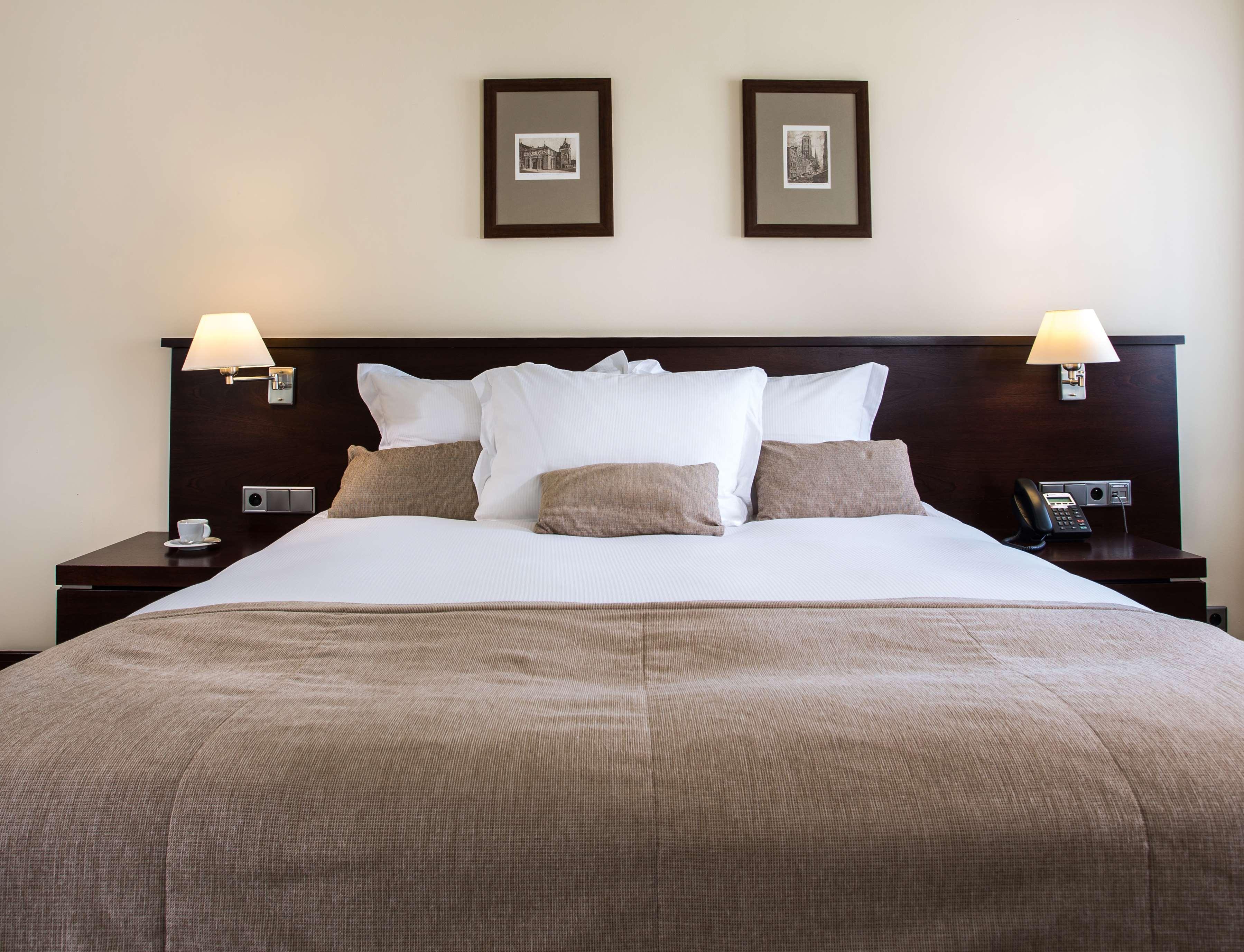 Radisson Blu Hotel, Gdansk Bagian luar foto The photo shows a well-decorated hotel room, focusing on a large bed with a dark wood headboard. The bed is adorned with several white pillows and a couple of beige cushions. There are two lamps on either side of the bed, providing soft lighting. Abo