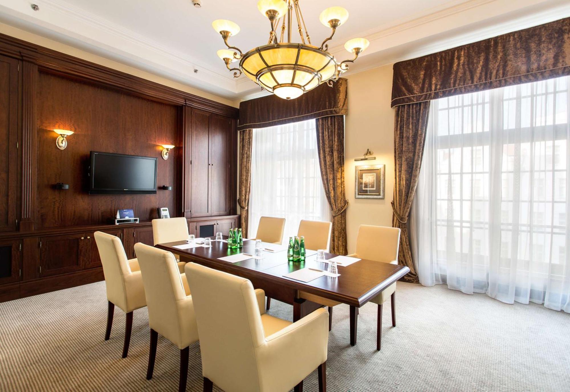 Radisson Blu Hotel, Gdansk Bagian luar foto The photo shows a well-furnished conference room. It features a large wooden table surrounded by six cream-colored chairs. On the table, there are several green glass bottles of water. The room is well-lit with a decorative chandelier hanging from th