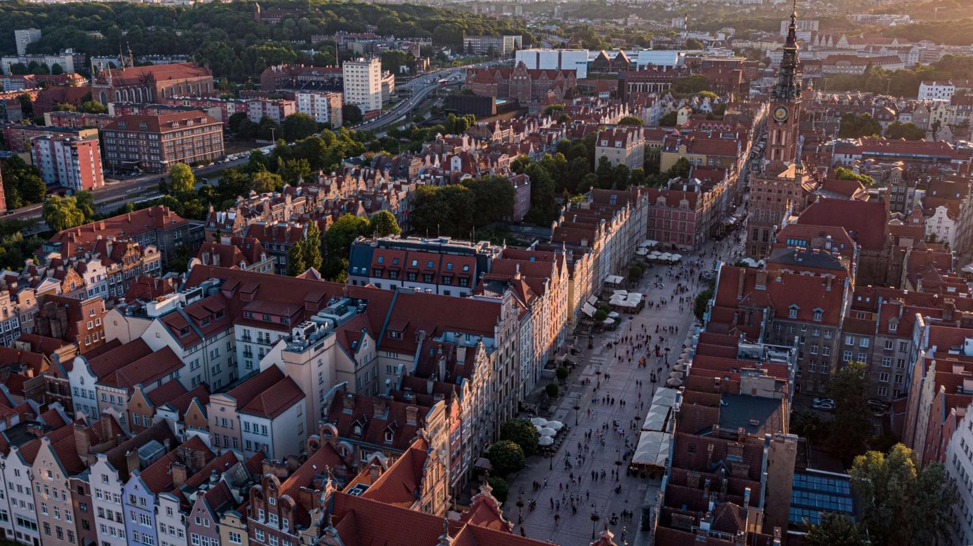 Radisson Blu Hotel, Gdansk Bagian luar foto The photo depicts a scenic aerial view of a city, likely Gdańsk in Poland. The landscape features historical buildings with distinctive architecture, characterized by colorful facades and prominent rooftop designs. A bustling street runs through the 